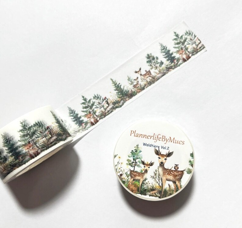 Op de afbeelding: Een rol washi tape met een witte achtergrond en een herhalend patroon van bossc&egrave;nes met herten, bomen en vogels. De tape is gelabeld "PlannerlifeByMues Waldtiere Vol. 2".