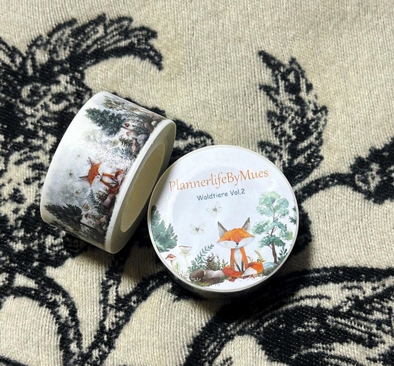 Op de afbeelding: Twee rollen washi tape met afbeeldingen van bosdieren. De eerste rol heeft een witte achtergrond met een besneeuwde bos sc&egrave;ne en een vos. De tweede rol heeft een witte achtergrond met een vos die in een bos zit met groene bomen en paddenstoelen. De tekst op de tweede rol is "PlannerlifeByMues Waldtiere Vol.2".