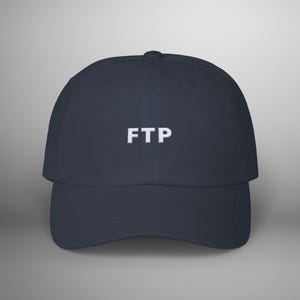 Op de afbeelding: Een donkerblauwe baseballpet met witte geborduurde tekst die "FTP" luidt.