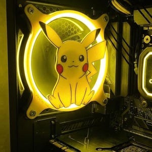 May include: A yellow Pikachu-themed computer fan with a glowing yellow outline. The fan is mounted inside a computer case, with other components visible. The fan has the text "Pikachu Fan" on it.