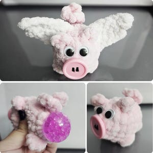 Puede incluir: Un cerdito de peluche rosa y blanco hecho a mano con grandes ojos saltones y una nariz de botón. El cerdo tiene alas blancas, lo que le da una apariencia caprichosa. El peluche está hecho de un material suave y texturizado.