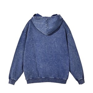 K&ouml;nnte beinhalten: Ein blauer Kapuzenpullover mit einem verblassten, abgenutzten Look. Der Pullover hat eine lockere Passform und eine Kapuze mit Kordelzug.
