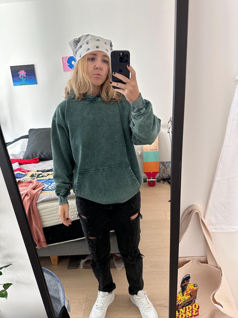 K&ouml;nnte beinhalten: Eine Person tr&auml;gt ein gr&uuml;nes Kapuzenpullover, eine schwarze zerrissene Jeans und wei&szlig;e Turnschuhe. Sie tr&auml;gt ein wei&szlig;es Bandana mit einem schwarzen Paisley-Muster auf dem Kopf. Die Person macht ein Selfie in einem Spiegel.