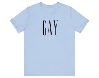 May include: A light blue short-sleeved t-shirt featuring the word GAY printed in a tall, black, serif-style font centred on the chest. The garment has a classic crew neckline and a standard fit, providing a simple and direct visual design.