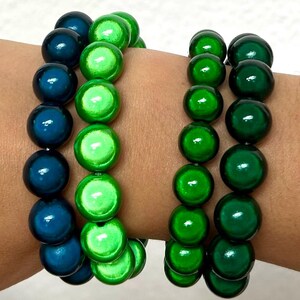 Könnte beinhalten: Zwei Perlenarmbänder mit runden, glänzenden Perlen. Das linke Armband besteht aus einem Strang dunkelblauer Perlen und einem Strang hellgrüner Perlen. Das rechte Armband besteht aus zwei Strängen dunkelgrüner, glänzender Perlen.