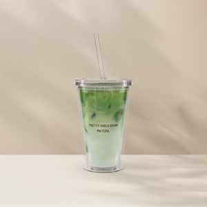 Könnte beinhalten: Ein klarer Kunststoffbecher gefüllt mit einem geschichteten grünen und weißen Getränk, gekrönt von einem klaren Strohhalm. Der Text "PRETTY GIRLS DRINK MATCHA." ist auf der Vorderseite aufgedruckt. Das Getränk ist ein Matcha Latte.