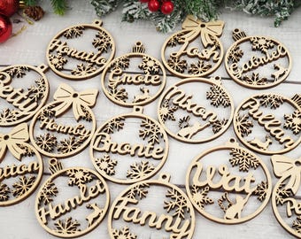 May include: Wooden Christmas ornaments with names like "Horatio", "Josh", and "Betty" are displayed. Each ornament is circular with a decorative snowflake and name cut-out design. Some have bow accents.