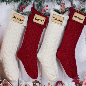 Peut inclure: Quatre bas de Noël personnalisés en tricot torsadé crème et rouge, chacun avec une étiquette nominative en bois. Les noms sont Marlon, Baird, Mandel et Walton. Décorations de vacances festives avec de la verdure et un bonhomme de neige en bois.