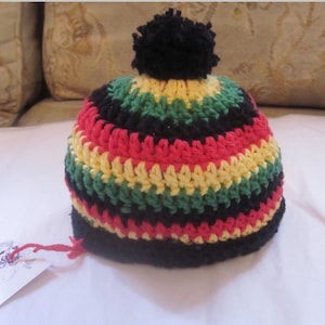 Puede incluir: Un gorro de punto con un pompón negro en la parte superior. El gorro está rayado con hilo rojo, amarillo, verde y negro.