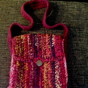 May include: A handmade, crocheted shoulder bag in a vibrant mix of red, pink, orange, and yellow yarns. The bag features a flap with a button closure and a long strap. The bag's dimensions are approximately 7 inches wide and 8 inches tall.