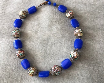 May include: A blue and brown glass bead necklace with a floral pattern. The necklace is made of round beads with a metallic finish.