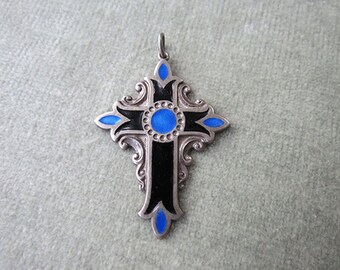 May include: A silver cross pendant with black and blue enamel. The cross has a decorative design and a central blue circle.