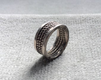 May include: A silver ring with a braided design. The ring is thick and has a wide band.