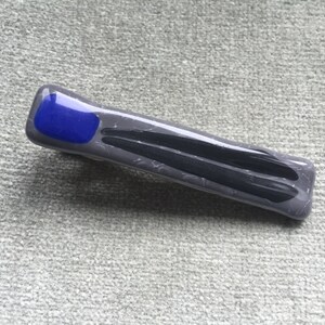 May include: A gray glass hair clip with a blue square accent.