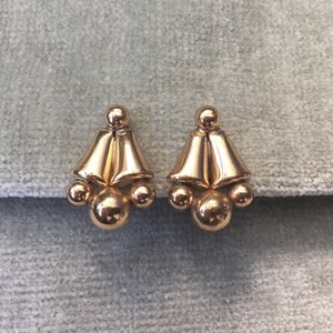May include: A pair of gold-toned earrings with a bell-shaped design and three round beads on each earring.