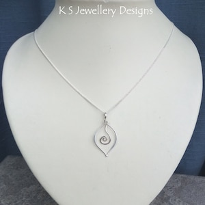 May include: A silver-toned necklace with a delicate pendant. The pendant features a wire-framed leaf shape with an interior spiral design. The necklace is displayed on a white mannequin. The text "K S Jewellery Designs" is visible at the top.