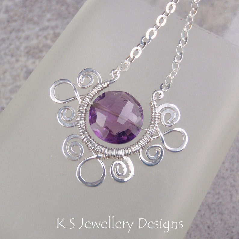 May include: A silver necklace with a purple amethyst gemstone pendant. The pendant is surrounded by silver wire that is twisted into a decorative design.