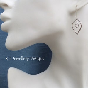 May include: A single silver earring with a teardrop shape and a spiral design. The earring hangs from a thin wire. The text "K S Jewellery Designs" is visible in the image.