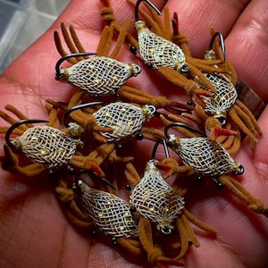 May include: A collection of handmade fishing flies. Each fly features a woven, cage-like body with gold accents, attached to a curved hook. The flies have brown, fuzzy legs and red tips, designed to mimic insects. The flies are designed for fly fishing.