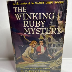 Op de afbeelding: De omslag van een vintage paperback boek getiteld "The Winking Ruby Mystery" door Carolyn Keene. Het boek maakt deel uit van de Dana Girls Mystery Stories-serie. De omslag toont een illustratie van twee meisjes die voor een spookachtig, oud gebouw staan.