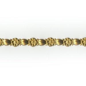 May include: A gold-colored decorative trim with a repeating pattern of oval shapes and floral designs. The trim is displayed against a white background, highlighting its intricate details and metallic sheen. This trim is suitable for various craft and design projects.