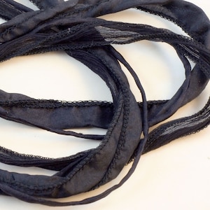 May include: Black silk ribbon with a textured edge. The ribbon is folded and twisted, creating a decorative effect.