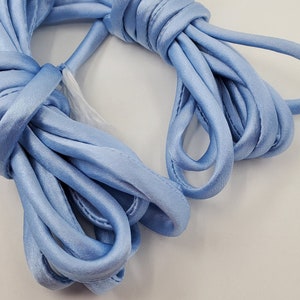 May include: A spool of light blue satin ribbon. The ribbon is soft and silky, and it is perfect for crafting, decorating, or adding a touch of elegance to any project.
