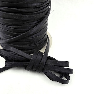 May include: A spool of black satin ribbon featuring a smooth, flat texture and a slight sheen. The ribbon is tightly wound around a central core, with a loose end extending forward and folded into a small loop, showcasing the consistent width.