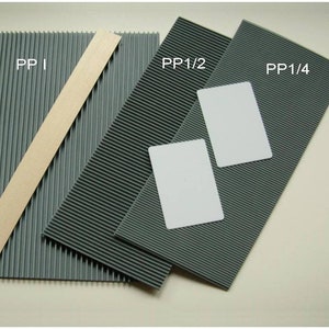 May include: An assortment of gray corrugated plastic sheets and a beige strip, labeled "PP 1", "PP 1/2", and "PP 1/4". Two white rectangular cards are on the rightmost sheet. The sheets have parallel ridges.