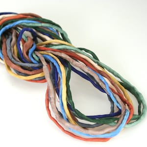 May include: A collection of colorful silk cords in shades of blue, green, brown, and yellow. The cords are arranged in a loose circle, with the ends overlapping.