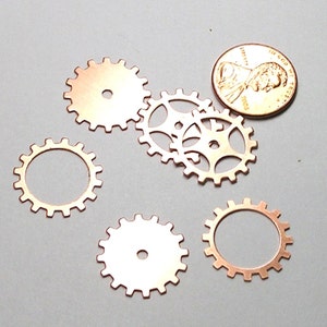 May include: Five copper gears of different sizes and designs. The gears are arranged in a semi-circle with a US penny in the center.