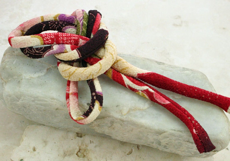May include: A knotted cord of fabric with a floral pattern in shades of red, white, brown, and green. The cord is tied in a decorative knot and the ends are hanging loose.