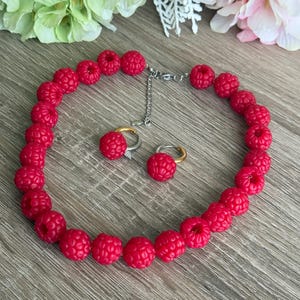 Peut inclure: Un collier et une paire de boucles d'oreilles créoles ornés de perles rouges sphériques et texturées rappelant des framboises. Le collier comprend une chaînette d'extension en métal argenté avec un fermoir mousqueton et des créoles dorées.