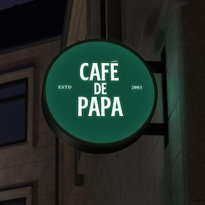 May include: A green round sign with white text that reads "Café de Papa" with "ESTD 2003" on either side of the text.