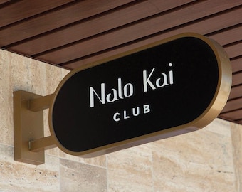 May include: A black and gold oval sign with the text "Nalo Kai CLUB" in white lettering. The sign is mounted on a tan wall with a brown wooden ceiling in the background.