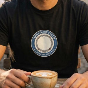 May include: A white ceramic mug with a black handle and the text "But First, Coffee" in a handwritten style. The mug is on a white surface. The mug is approximately 10 cm tall.