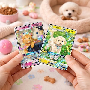 May include: Two trading cards are held up, featuring cartoon animals. One card has an orange cat named "Jack" and the other has a white dog named "Stella". The cards have a holographic design with the year "2026" and other text. A small dog is in the background.