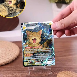 May include: A rectangular trading card featuring a brown tabby cat illustration with lightning effects. The card text reads Gabby VMAX, 2026 HP, Nap Ninja, and Purring Heal. The card is displayed on a clear plastic stand, showing a holographic finish.