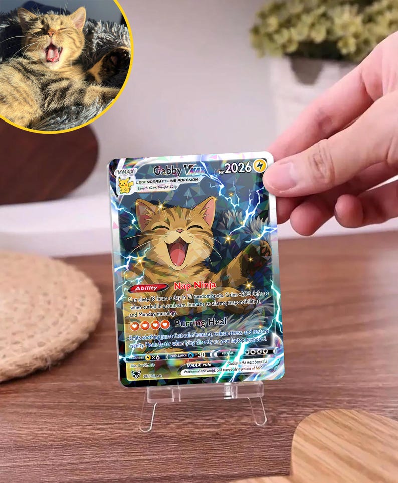 May include: A rectangular trading card featuring a brown tabby cat illustration with lightning effects. The card text reads Gabby VMAX, 2026 HP, Nap Ninja, and Purring Heal. The card is displayed on a clear plastic stand, showing a holographic finish.