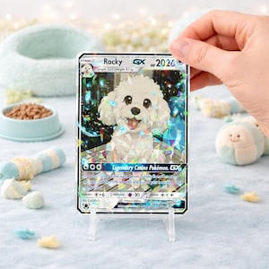 May include: A Pok&eacute;mon trading card featuring "Rocky," a white dog illustration with the text "Legendary Canine Pok&eacute;mon. GX." The card is held in a clear stand, with a light blue background and dog-themed accessories.