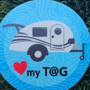 May include: A blue and white sticker with a cartoon image of a small camper trailer. The sticker has a red heart and the text "my T@G" on it.