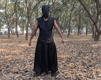 May include: A black sleeveless vest with a wide waistband and a long, pleated skirt. The outfit includes a matching black head covering that obscures the face, creating a uniform, dark, and structured appearance for the entire ensemble.