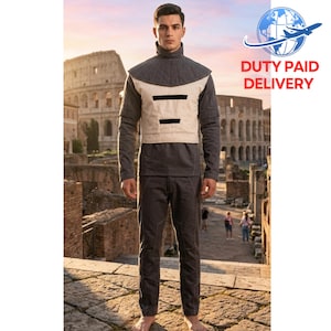 May include: A person wearing a grey and beige outfit with a high collar, standing in front of the Colosseum. The outfit includes a long-sleeved shirt, a vest with black accents, and matching trousers. The background features the ancient Roman amphitheatre.
