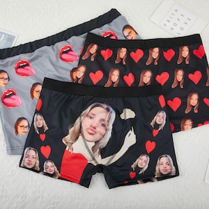 Può includere: Tre paia di boxer neri e grigi con una stampa di cuore rosso e viso. La stampa presenta diversi volti di persone.