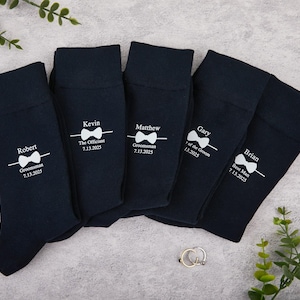 May include: Five navy blue socks, each with a white bow tie design and personalised text. The socks are labelled with names, roles, and dates: Robert, Groomsman, 7.13.2025; Kevin, The Officiant, 7.13.2025; Matthew, Groomsman, 7.13.2025; Gary, of the Groom, 7.13.2025; Brian, Best Man, 7.13.2025.