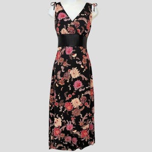 May include: A black floral print dress with a V-neckline and a black belt. The dress features a pattern of pink, red, and cream-colored flowers. The straps are tied at the shoulders.