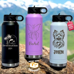May include: Three stainless steel water bottles with different designs and names. The first bottle is black with a palm tree and dolphin design and the text "Destination 2024". The second bottle is purple with a butterfly design and the name "Rachel". The third bottle is light gray with a Yorkshire Terrier design and the name "John".