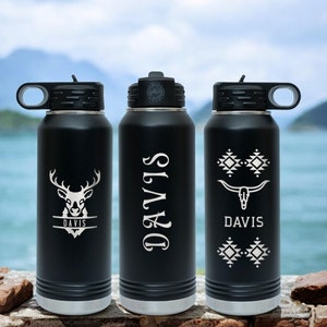 May include: Three black stainless steel water bottles with different designs. The first bottle has a deer head with the name "DAVIS" underneath. The second bottle has the name "DAVIS" in a vertical script font. The third bottle has a skull with horns and a geometric pattern with the name "DAVIS" underneath.