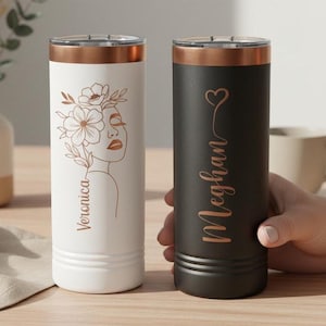 May include: Two insulated tumblers. One is white with a floral design and the name "Veronica" in a copper colour. The other is black with the name "Meghan" and a heart in copper. Both have copper-coloured rims.