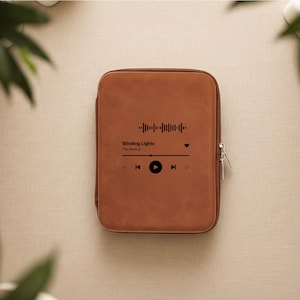 May include: A brown tablet case with a zipper closure. The case features a graphic of a song's waveform, play controls, and the text "Blinding Lights" by The Weeknd.